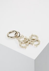 Złoty brelok w kształcie powiązanych okręgów. Gładkie metalowe wykończenie o błyszczącej fakturze oraz zaokrąglona zawieszka na klucze.