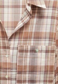 Camicia con colletto e bottoni, con un motivo a quadri beige, marrone e bianco, e una tasca sul petto con bottone sul lato destro.