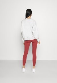 Grå sweatshirt med hängande axlar, kombinerad med tighta vinröda leggings. Vita sneakers. Enkla bakgrund, neutrala färger.