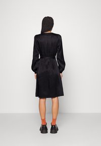 Černé šaty s dlouhými rukávy, úzkým pasem a rozšířenou sukní. Vyrobené z hladkého materiálu, s texturovaným designem a odpovídajícím páskem.