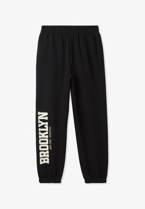 Joggers neri in cotone con vita e polsini elastici. "BROOKLYN" stampato in lettere crema in grassetto lungo la gamba sinistra. Fit semplice e rilassato.