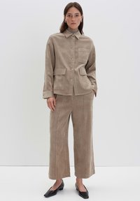 Completo in corda beige composto da una camicia con bottoni e quattro tasche e pantaloni a gamba larga. La texture è morbida e con una leggera lucentezza.