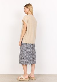 Beige oversized stickad topp med korta ärmar, i kombination med en knälång mönstrad kjol med ett geometriskt blått och vitt mönster.