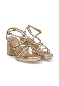 Sandalias de tacón alto metálicas doradas con tiras entrelazadas, tacón grueso y plantilla acolchada, que presentan un acabado suave y un diseño minimalista.