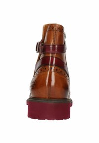 Bottine en cuir marron avec des brides bordeaux et une boucle. Présente des détails de brogue, une pointe ronde et une épaisse semelle bordeaux.