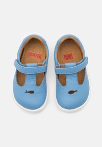 Blaue Lederschuhe mit runder Spitze und einem Riemen über dem Fuß, der ausgeschnittene Löcher aufweist. Braune Einlegesohlen und ein Fischdesign auf der Spitze.