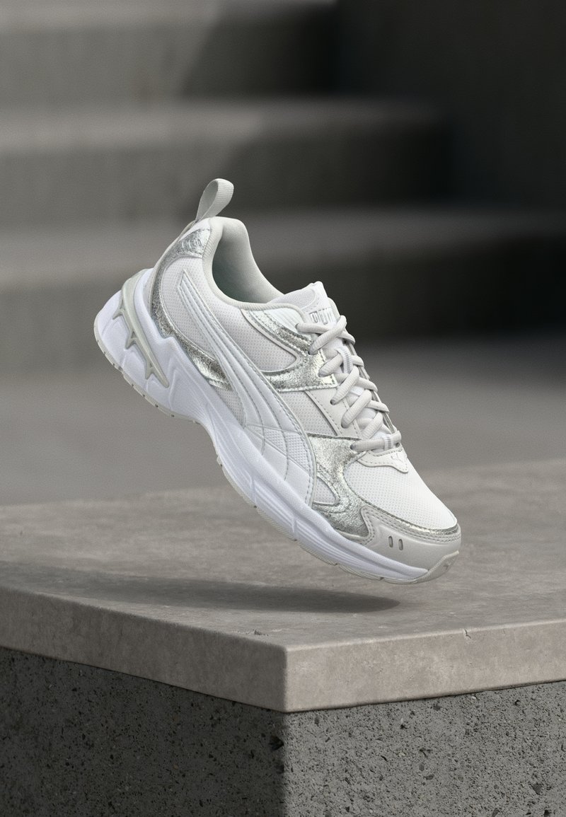 Άσπρο και ασημί αθλητικό παπούτσι κρεμασμένο πάνω από μια σκυρόδετη προεξοχή με θολές σκάλες στο παρασκήνιο.