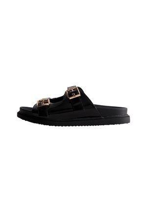 Sandalias de charol negro con dos correas ajustables, adornos de hardware dorado, suela gruesa y superficie texturizada para un mejor agarre.