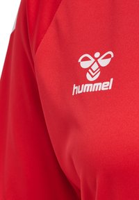 Rød sportstrøje med en glat tekstur, hvid "hummel" logo og et bi-design på venstre side.