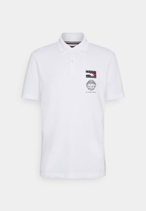 Polo blanc avec col, manches courtes et un motif sur le côté gauche de la poitrine. Il comporte un patch logo et un dessin de globe avec du texte.