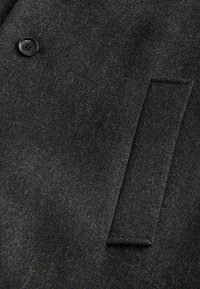 Mørkegrå uldfrakkefremstillet med et tekstureret stof, sort knap og et skrå pocket-design, der er skabt til varme og stil.