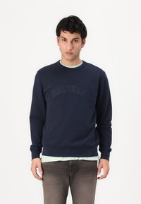 Felpa blu navy con collo a giro, caratterizzata da un logo "BELSTAFF" tono su tono sul petto. Tessuto morbido e polsini a costine per un comfort ottimale.