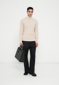 Hellbeige gerippter Rollkragenpullover, schwarze Hose, schwarze Leder-Umhängetasche mit mehreren Fächern und schwarze Schuhe.