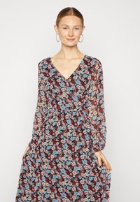 Vestido floral com mangas compridas e decote em V, apresentando um fundo preto e flores multicoloridas em tons de azul, rosa e vermelho.