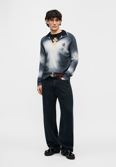 Πλεκτό πουλόβερ με βαθμωτό μπλε-γκρι χρώμα, μπροστινό γιακά και κεντημένο λογότυπο· συνδυασμένο με μαύρα τζιν πλατύποδα και λαμπερά μαύρα παπούτσια.