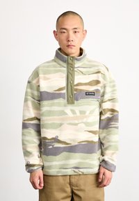 Pullover in pile di colore verde tenue, beige e grigio a motivo camouflage. Presenta un colletto alto, chiusura a bottoni e una piccola tasca sul petto con logo.
