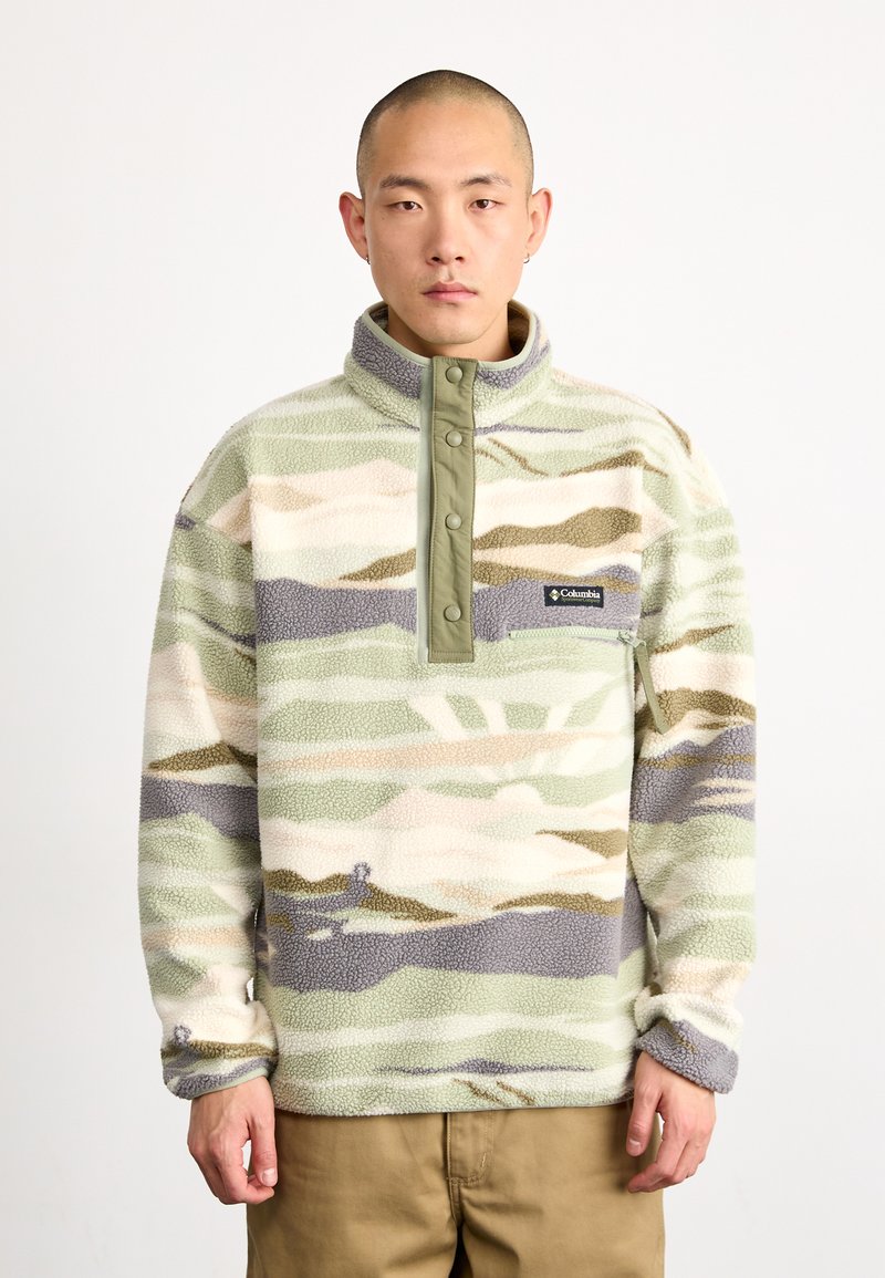 Pullover in pile di colore verde tenue, beige e grigio a motivo camouflage. Presenta un colletto alto, chiusura a bottoni e una piccola tasca sul petto con logo.
