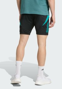 Black athletic shorts with teal accents and three stripes on the sides, paired with white socks and athletic shoes. Textured mesh top.
