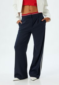 Pantalones de pierna ancha a rayas marino con una cinturilla a rayas rojas y blancas. Presenta pliegues frontales y bolsillos laterales. La tela tiene una textura suave.