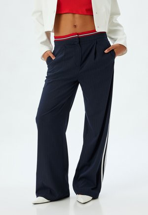 Pantalons larges à rayures marines avec une ceinture à rayures rouges et blanches. Comprend des plis sur le devant et des poches latérales. Le tissu a une texture lisse.