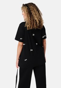 Zwarte t-shirt met korte mouwen en een ontspannen pasvorm, met witte strikaccenten verspreid op de rug en een rechte zoom.