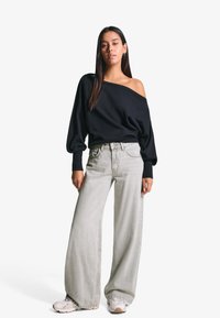 Fekete, vállnélküli pulóver, melynek bolyhos ujjai vannak, világosszürke, bő szárú farmernadrággal és fehér tornacipővel párosítva. Simaság tapintása.