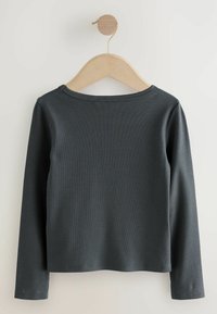 Haut à manches longues gris foncé en tissu côtelé, avec un col rond et une texture lisse. Suspendu sur un cintre en bois contre un fond clair.