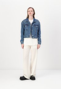 Denim-takki klassisella kauluksella, kaksi rintataskua ja napitus. Päällä valkoinen toppi ja vaaleanbeige leveälahkeiset housut. Mustat platform-kenkä.
