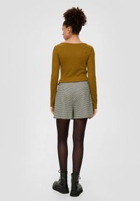 Rostfarbener, gerippter Langarm-Top, kombiniert mit karierter, hochgeschnittener Shorts. Das Modell trägt schwarze, klobige Stiefel und transparente schwarze Strumpfhosen.