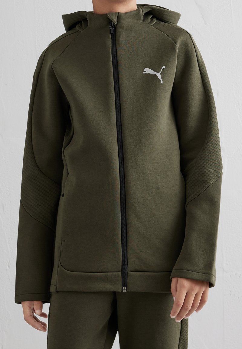 Olivengrøn hættetrøje med lynlås foran, strukturerede ærmer og et logo på brystet. Blødt stof med en afslappet pasform og sidelommer.