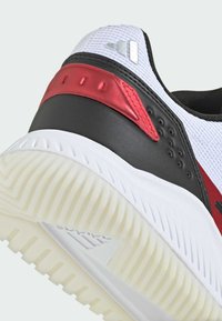 Chaussure de sport noir et blanc avec un dessus en mesh texturé, des accents synthétiques rouges et une semelle extérieure en caoutchouc blanc présentant des rainures prononcées.