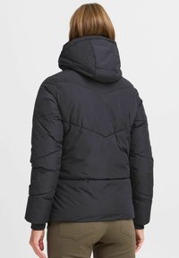 Veste noire rembourrée avec capuche, présentant des coutures en chevrons, des poignets élastiqués et un tissu lisse et résistant à l'eau.