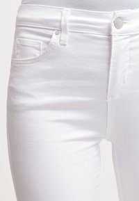 Vita denimjeans med slim fit, femfickorsdesign och knappknäppning framtill. Tyget har en slät yta med minimal detaljering.