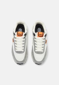 Paire de baskets FILA blanches et grises avec des écussons de logo orange et des lacets blancs, vues de dessus sur un fond uni.