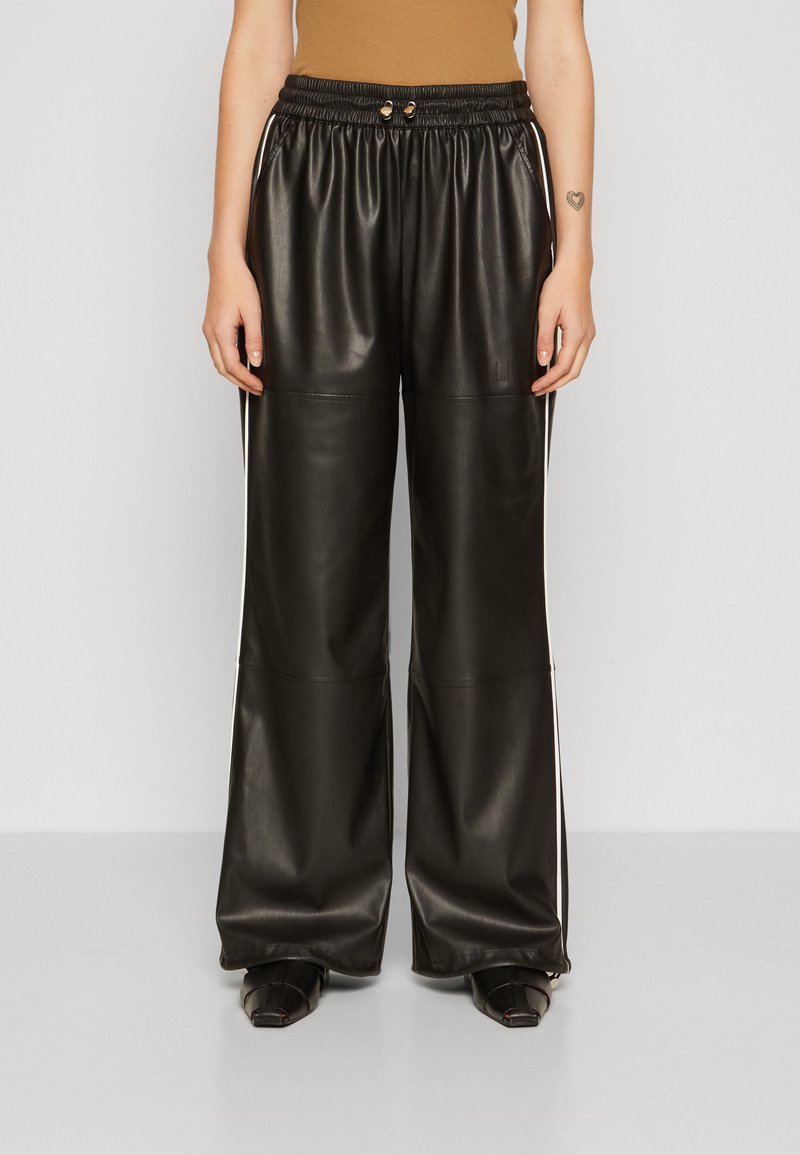 Pantalones anchos de imitación de cuero negro con cinturilla elástica, que presentan rayas laterales blancas. Textura suave y detalles de diseño minimalistas.