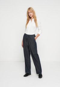 Balta mygtukais užsegama palaidinė derinama su tamsiais džinso kelnėmis su elastine juosmens juosta, šoninėmis kišenėmis ir laisvu siluetu. Juodi batai užbaigia derinį.