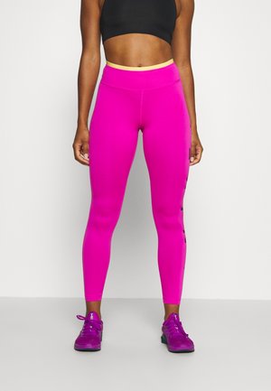 Leggings de sport ajustés en rose vif avec une taille haute dotée d'une bande intérieure jaune contrastante, associés à des chaussures de sport violettes.