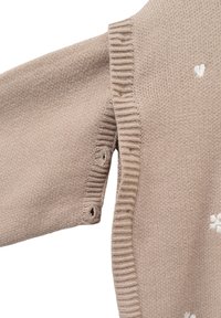 Maglione beige lavorato a maglia con scollo a costine. Presenta piccoli motivi a forma di cuore bianchi, aperture con bottoni sui lati con bordi arrotondati.