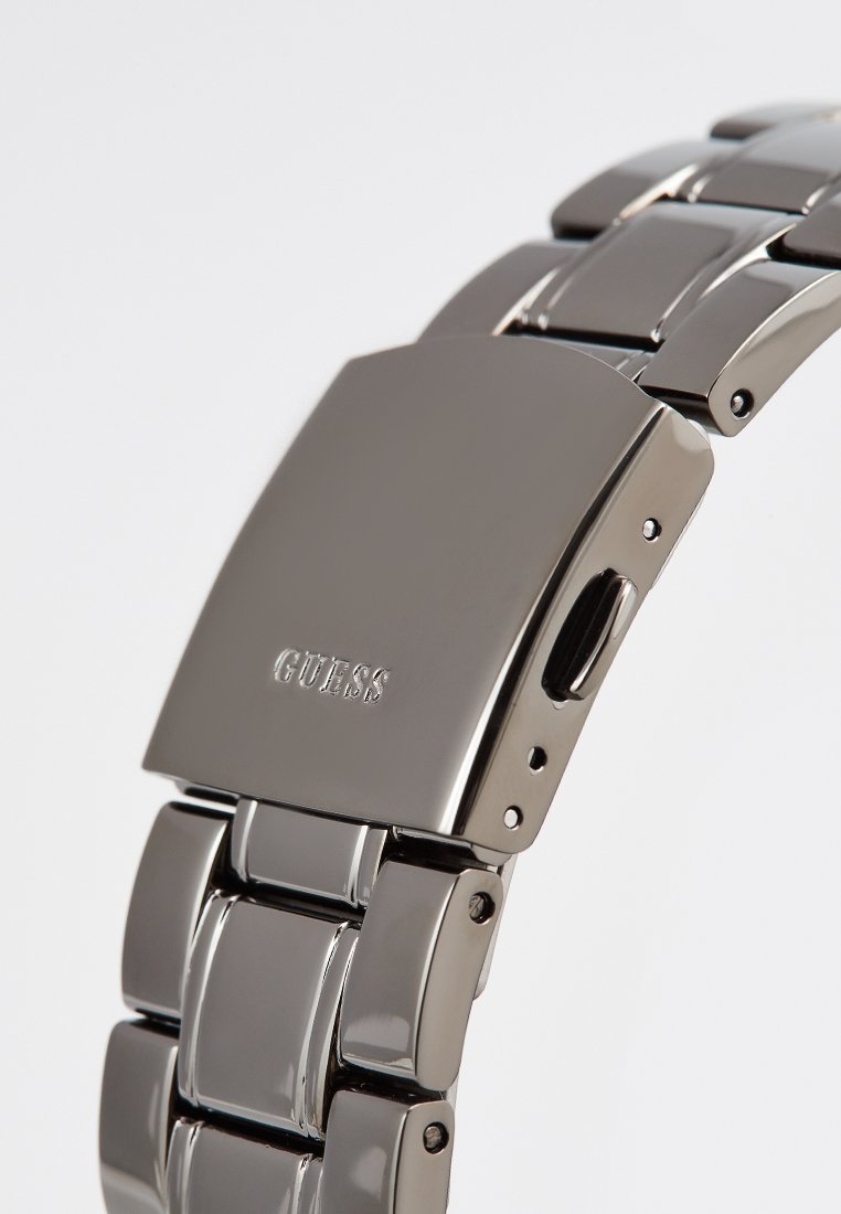 Srebrny zegarek ze stali nierdzewnej o polerowanej powierzchni, z prostokątną kopertą i bransoletą z ogniw, wytłoczonym logo "GUESS".