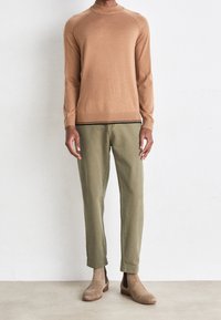 Strickpullover in Kamel-Farbe mit Rundhalsausschnitt und gerippten Bündchen, kombiniert mit grünen Chinos und hellbraunen Wildleder-Ankle-Boots.