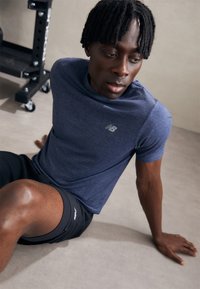 T-shirt de sport à manches courtes de couleur marine avec un logo discret, associé à un short noir. Le tissu semble léger et respirant, adapté à l'exercice.