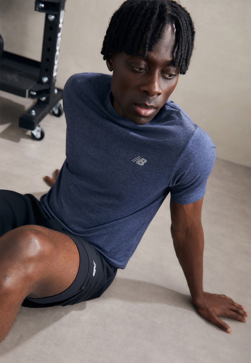 T-shirt de sport à manches courtes de couleur marine avec un logo discret, associé à un short noir. Le tissu semble léger et respirant, adapté à l'exercice.