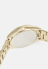 Reloj de acero inoxidable dorado con una caja redonda, bisel liso y una pulsera de eslabones. Presenta una corona para ajustes y un dial minimalista.