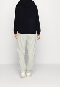 Felpa navale con cappuccio, abbinata a pantaloni della tuta grigio chiaro. I pantaloni sono larghi e si stringono alle caviglie. Si indossano sneaker bianche.