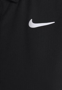 Svart atletisk tyg med ett strukturerat mönster, med en vit Nike-logotyp på bröstområdet. Designen är minimalistisk och åtsittande.