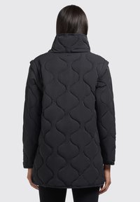 Manteau matelassé noir avec col haut, couture en motif vague et manches longues, conçu pour la chaleur et la couverture.