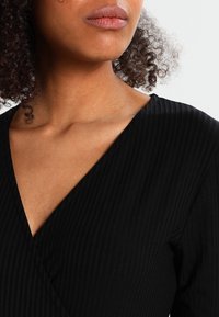 Svart ribbad topp med djup V-ringning, långa ärmar och en texturerad väv, som betonar en figurnära silhuett.
