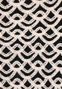 Svart texturerad tyg med ett vitt virkade mönster av sammanflätade kurvor och diamanter, som skapar en upprepande geometrisk design.
