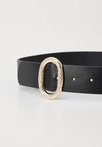 Mustavartsainen nahkavyö, jossa on teksturoitu kultainen soikea solki ja useita säätöreikiä. Vyön pinta on sileä ja siinä on hienovarainen kiilto.