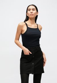 Černý žebrovaný tílko spárované s texturovanou černou sukní na knoflíky s kapsami a přiléhavým střihem. Hladká látka a krátká délka.